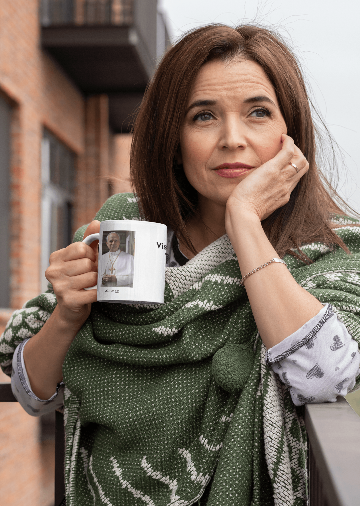 Mujer sosteniendo la taza conmemorativa de la visita del Papa a España en un balcón exterior.