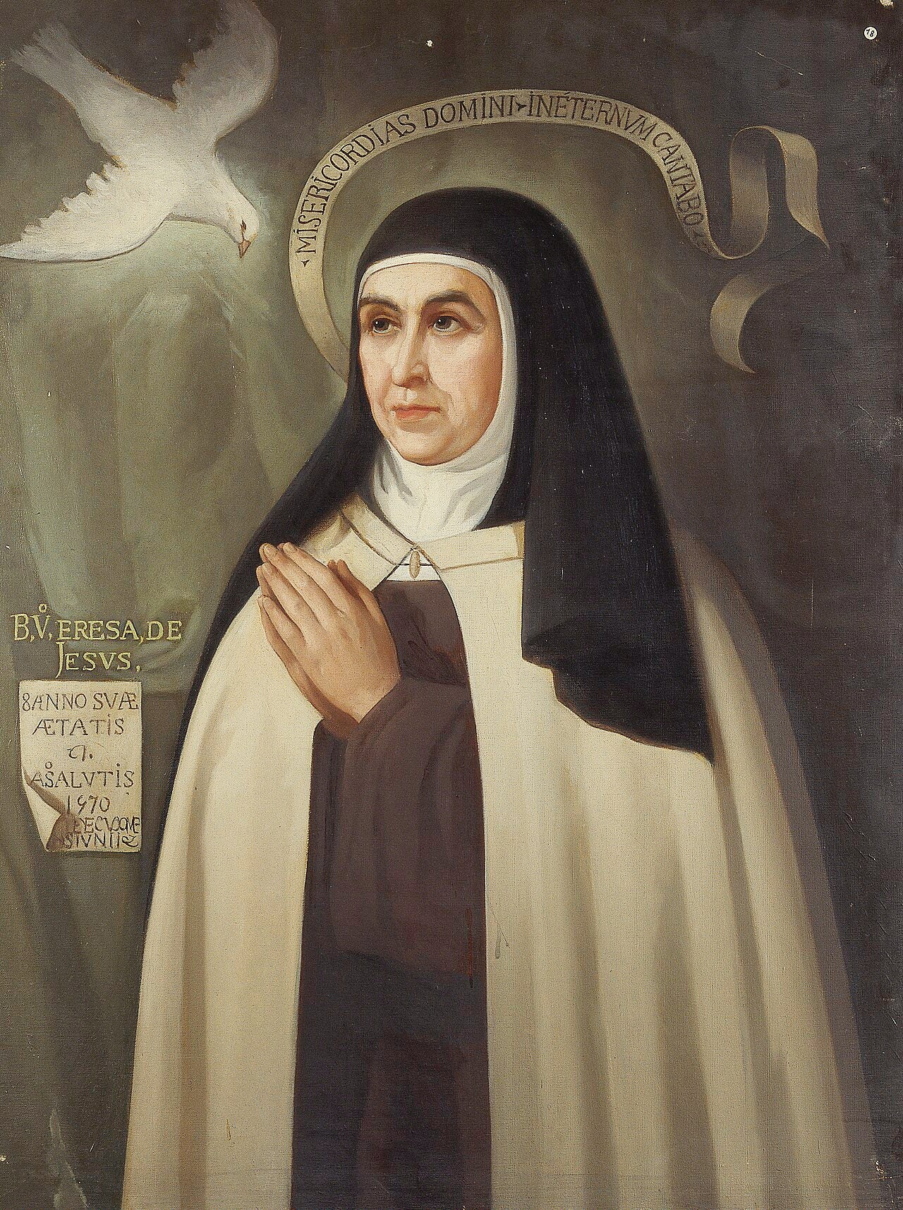 Pintura al óleo que retrata a Santa Teresa de Jesús con hábito carmelita y manto blanco, sentada junto a una mesa con una pluma y un libro abierto.