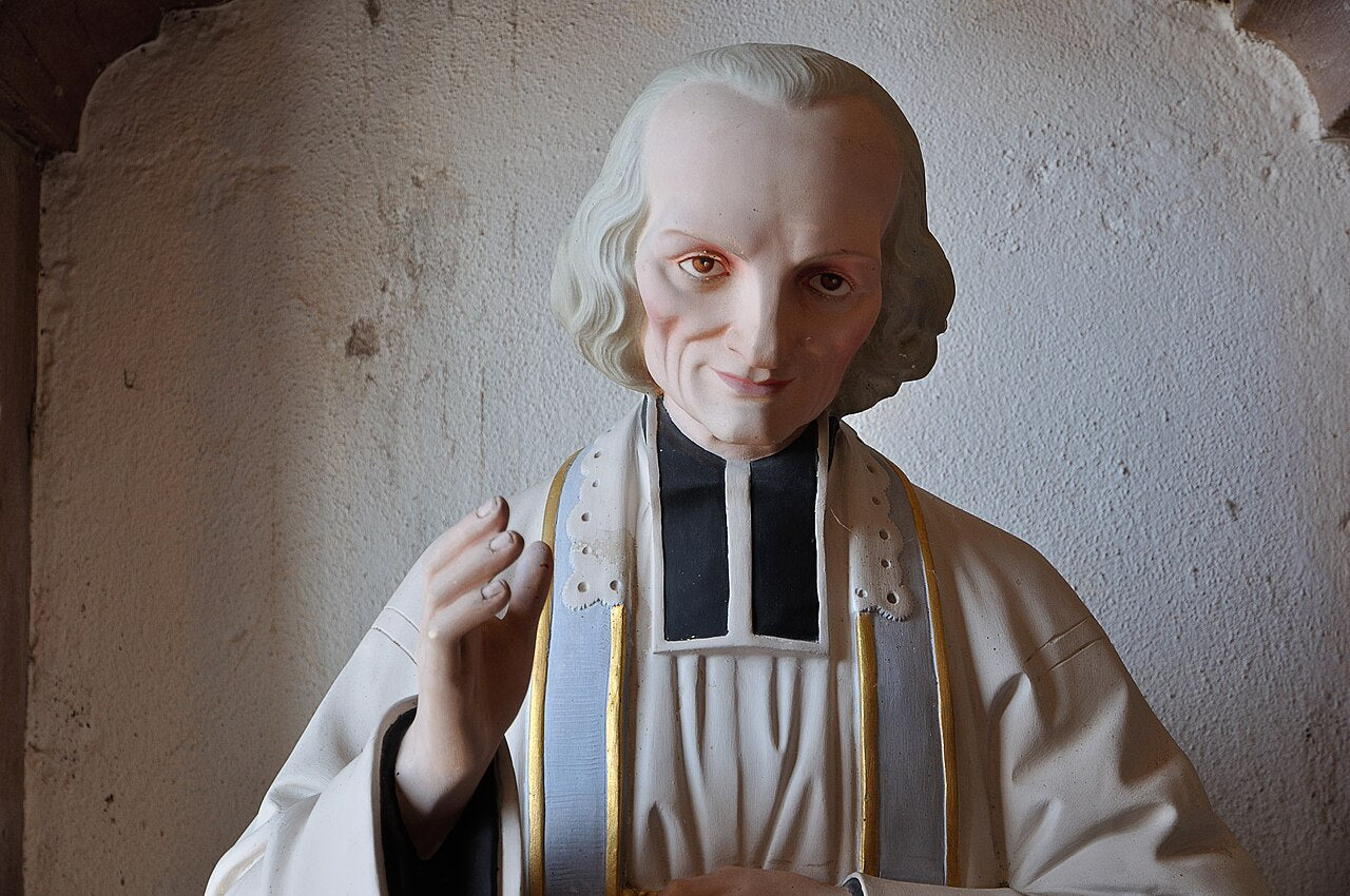 Estatua de San Juan María Vianney situada junto a una iglesia