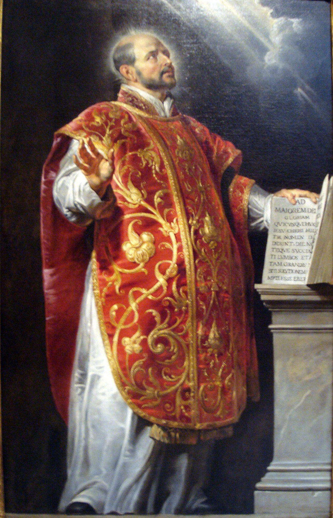 Pintura al óleo de San Ignacio de Loyola vistiendo casulla sacerdotal oscura y roja, mirando hacia arriba con expresión devocional.