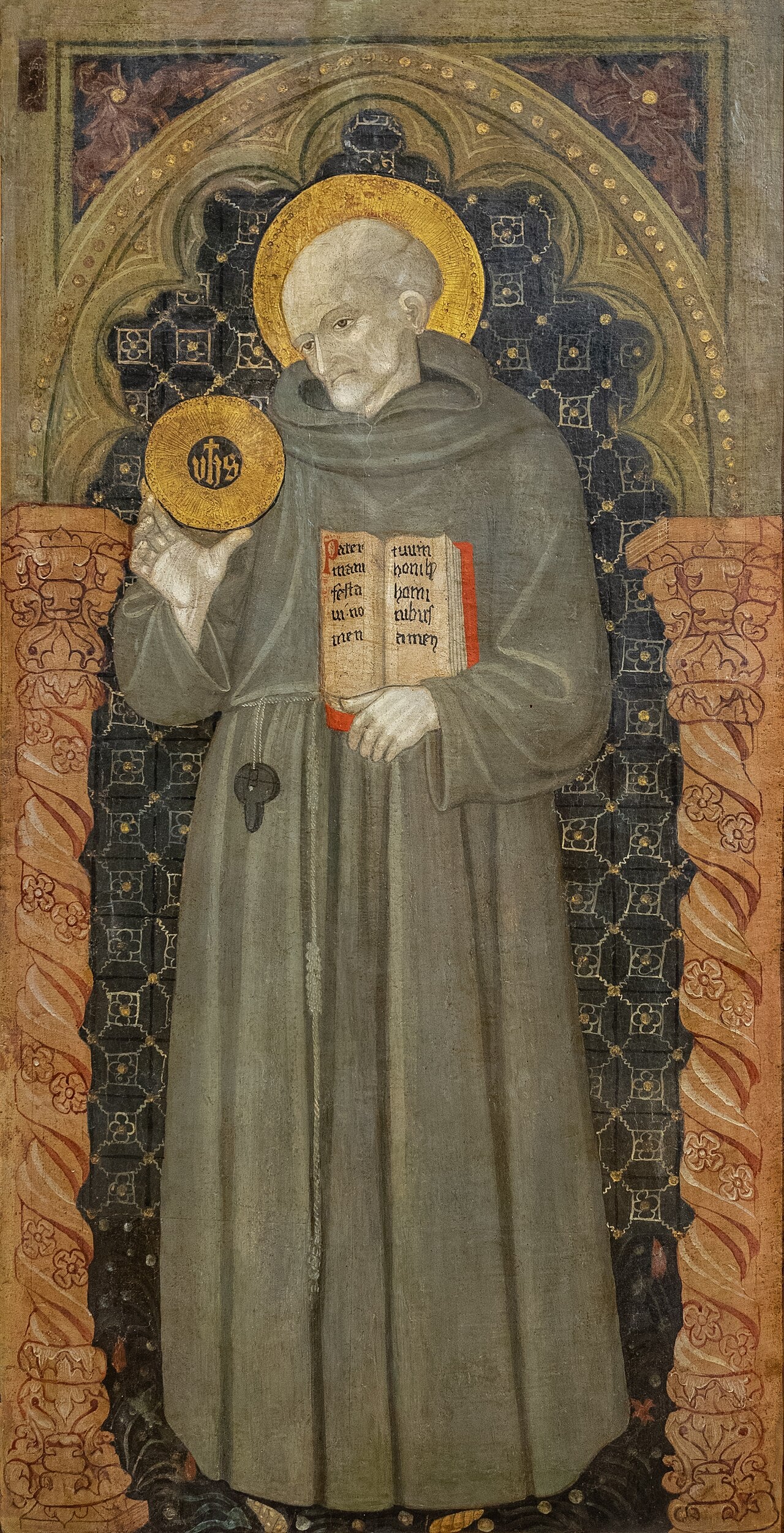 Pintura del siglo XV que representa a San Bernardino de Siena de cuerpo entero, con hábito franciscano y sosteniendo una tablilla con el cristograma IHS radiante.