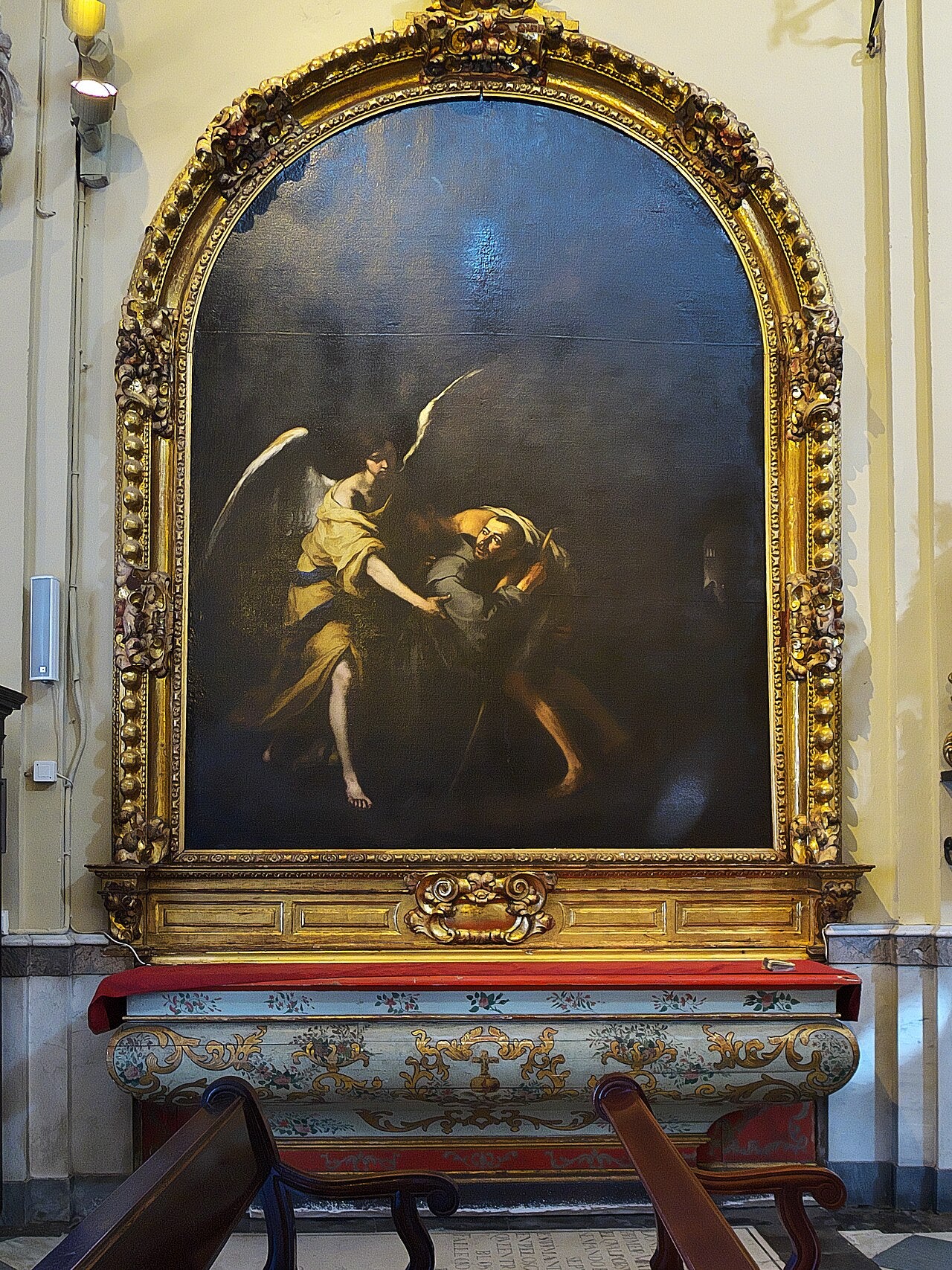 Pintura que representa a San Juan de Dios sosteniendo a una persona enferma, asistido por una figura angelical.