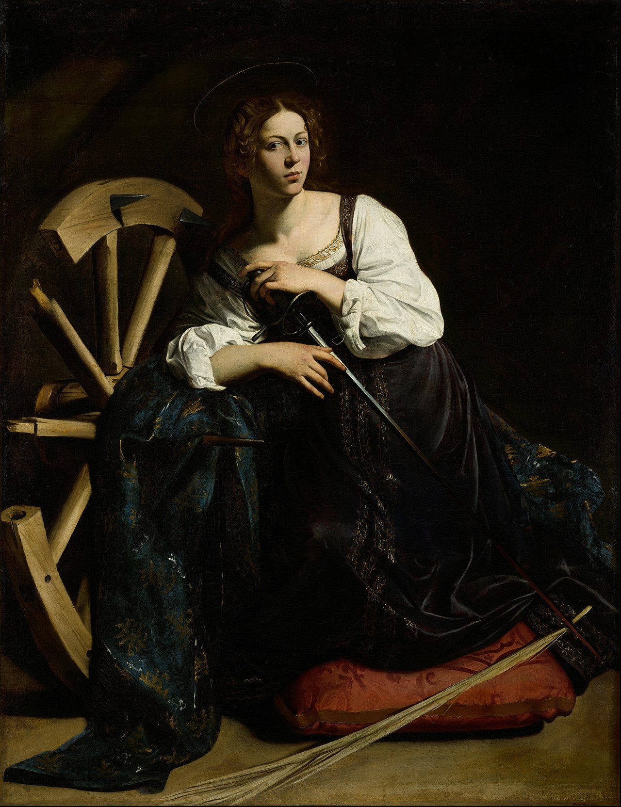 Pintura de Santa Catalina de Alejandría representada por Caravaggio, mostrando a la santa junto a una rueda dentada rota, una espada y la palma del martirio sobre un cojín bordado.