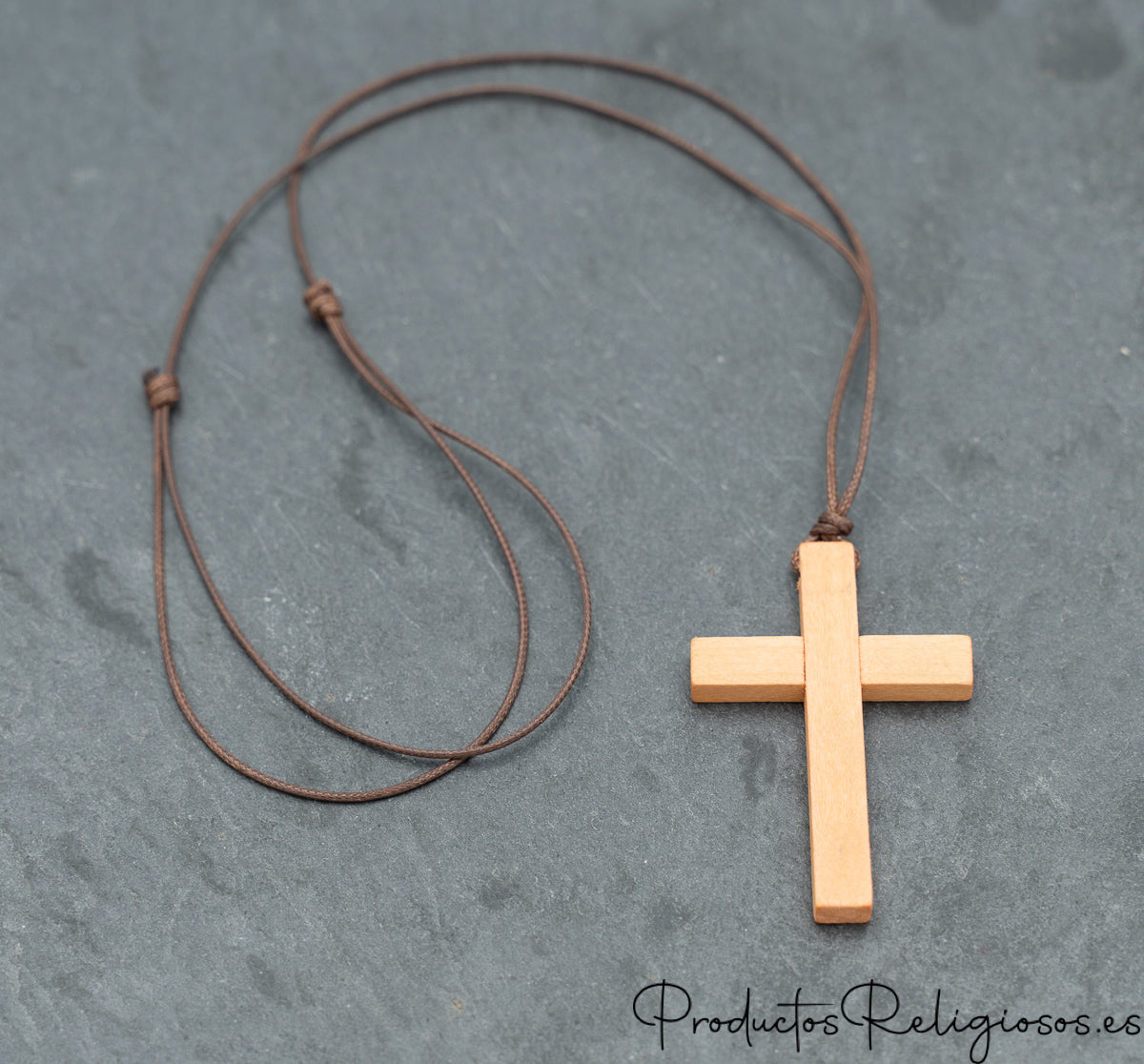 Colgante religioso de madera clara con cordón fino sobre fondo de piedra gris.